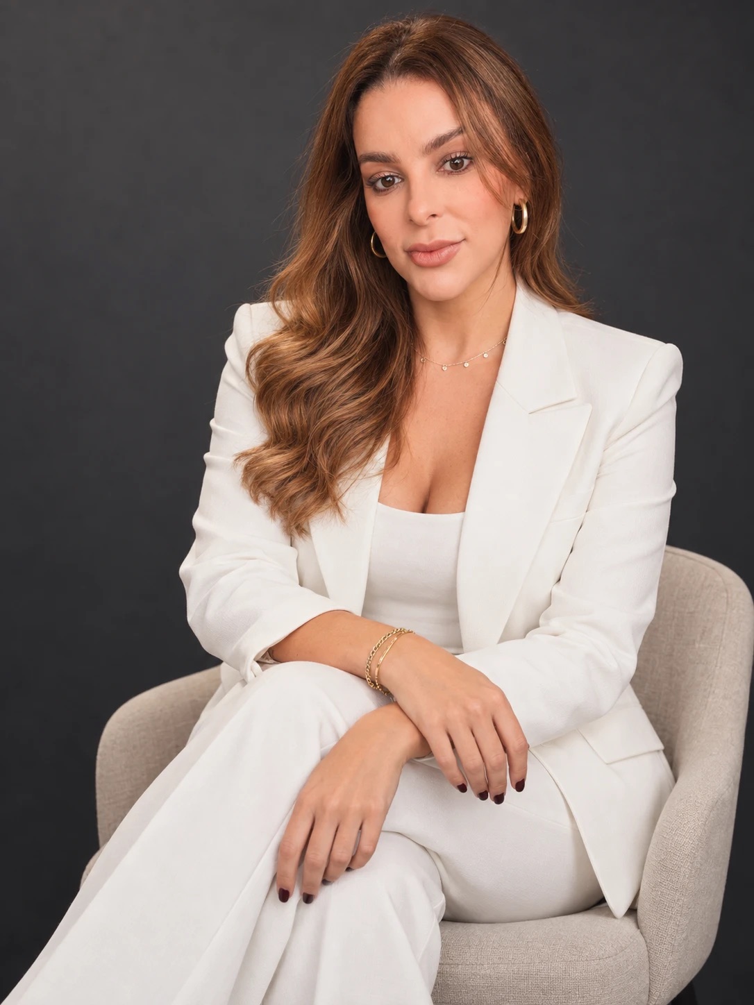 Ana Ralil, fundadora da Ralil Sport Business, sentada em uma poltrona, de terno branco